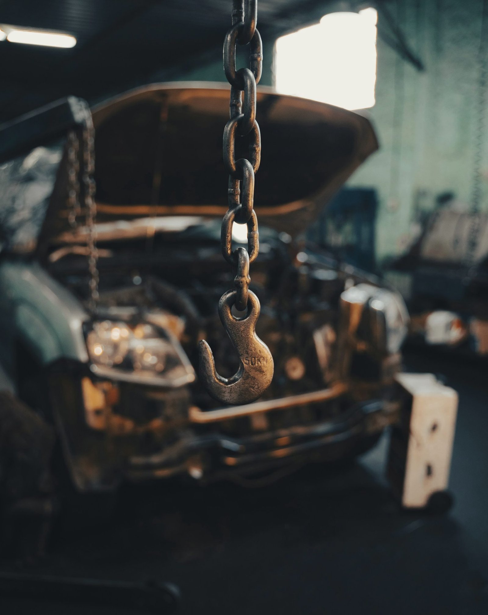An engine hanging from a chain hoist inside a dim workshop