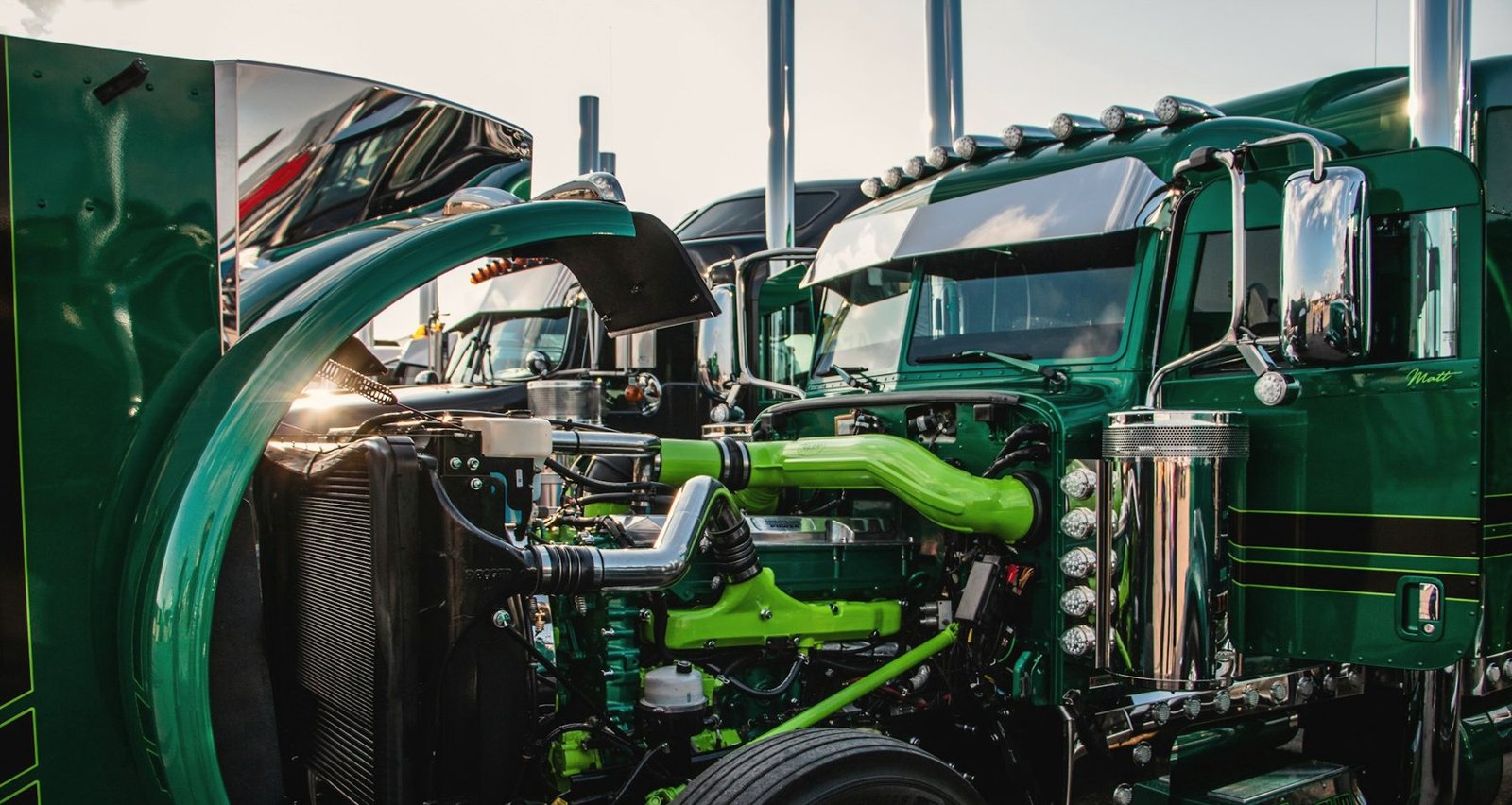 A green semi tractor with its hood tilted forward, showing the diesel engine