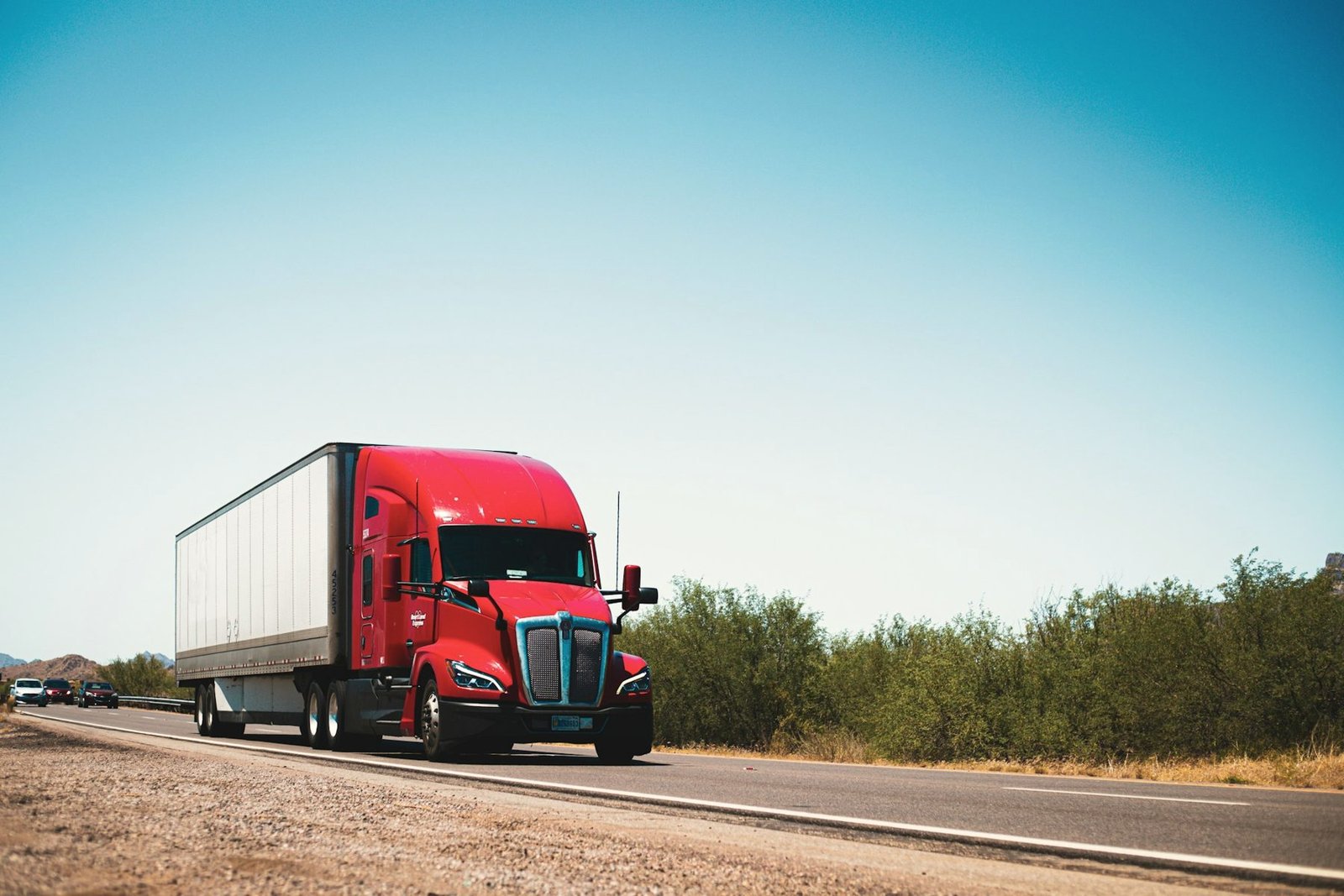 A red semi tractor pulling a white van trailer on a two-lane country road